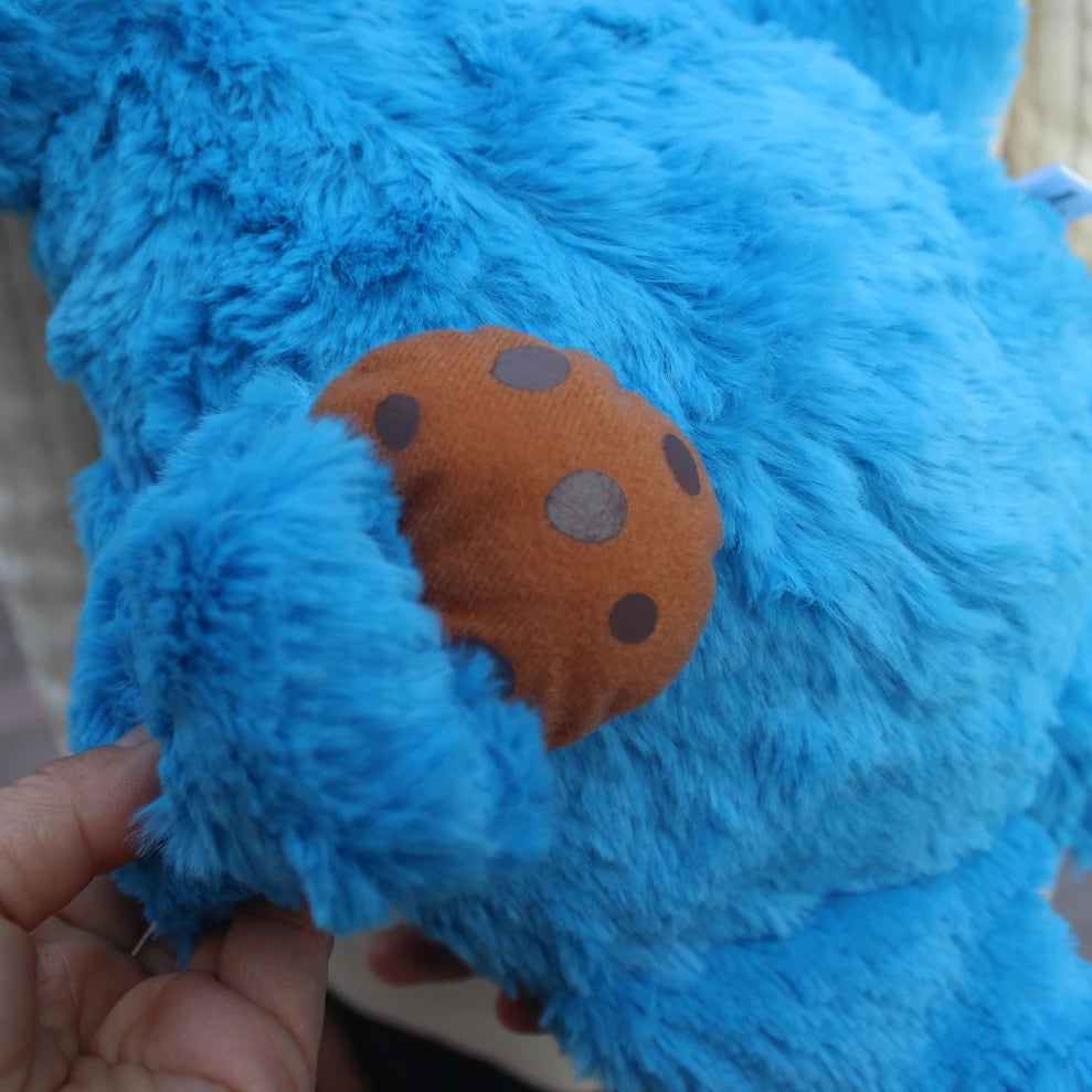 A hand is holding a blue Cookie Monster plush toy, showing an orange patch with brown polka dots.