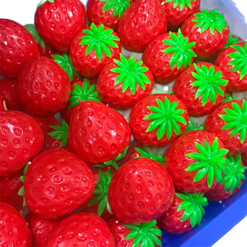 A close-up view of a pile of bright red strawberry stress balls with green leaves in a blue container.