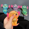 A hand holds an orange squishy axolotl stress relief toy with pink accents against a dark background.