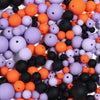 A close-up view of various matte acrylic beads in shades of orange, purple, and black scattered on a white surface.