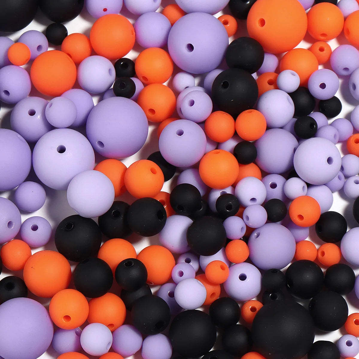 A close-up view of various matte acrylic beads in shades of orange, purple, and black scattered on a white surface.