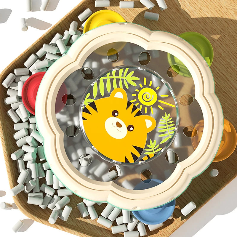 A clear plastic rattle and hand drum set with a yellow tiger design placed on a wooden tray surrounded by small white beads.