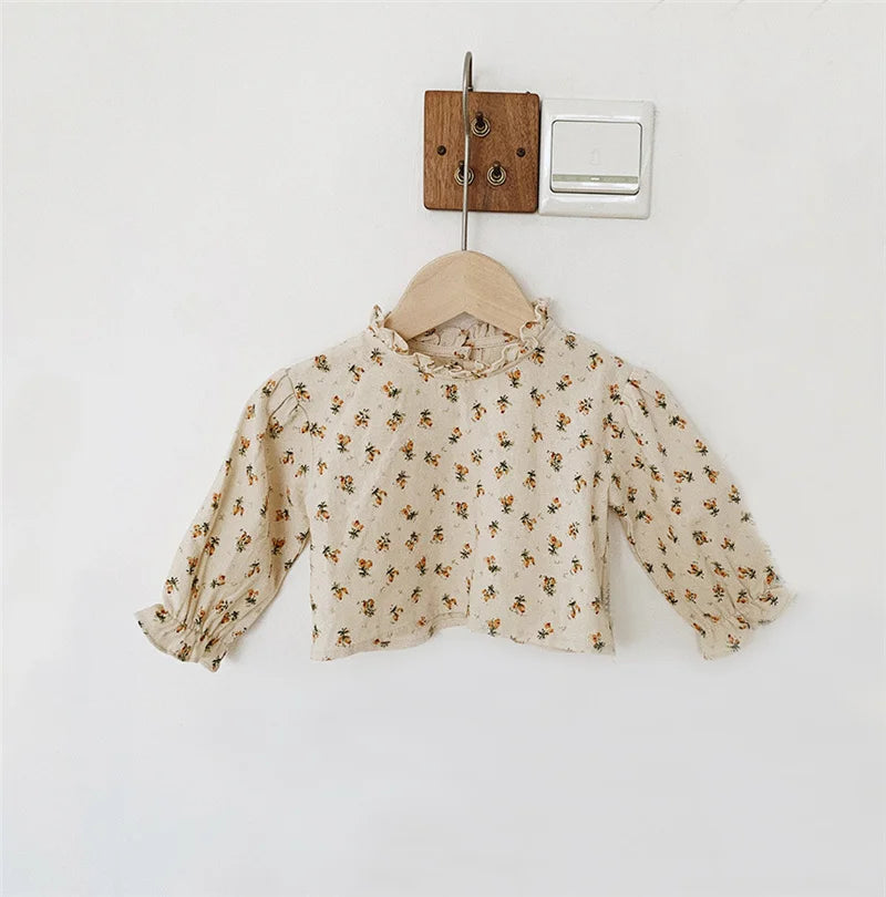 A light beige vintage floral baby girl outfit set featuring a blouse and romper, hanging on a wooden hanger.