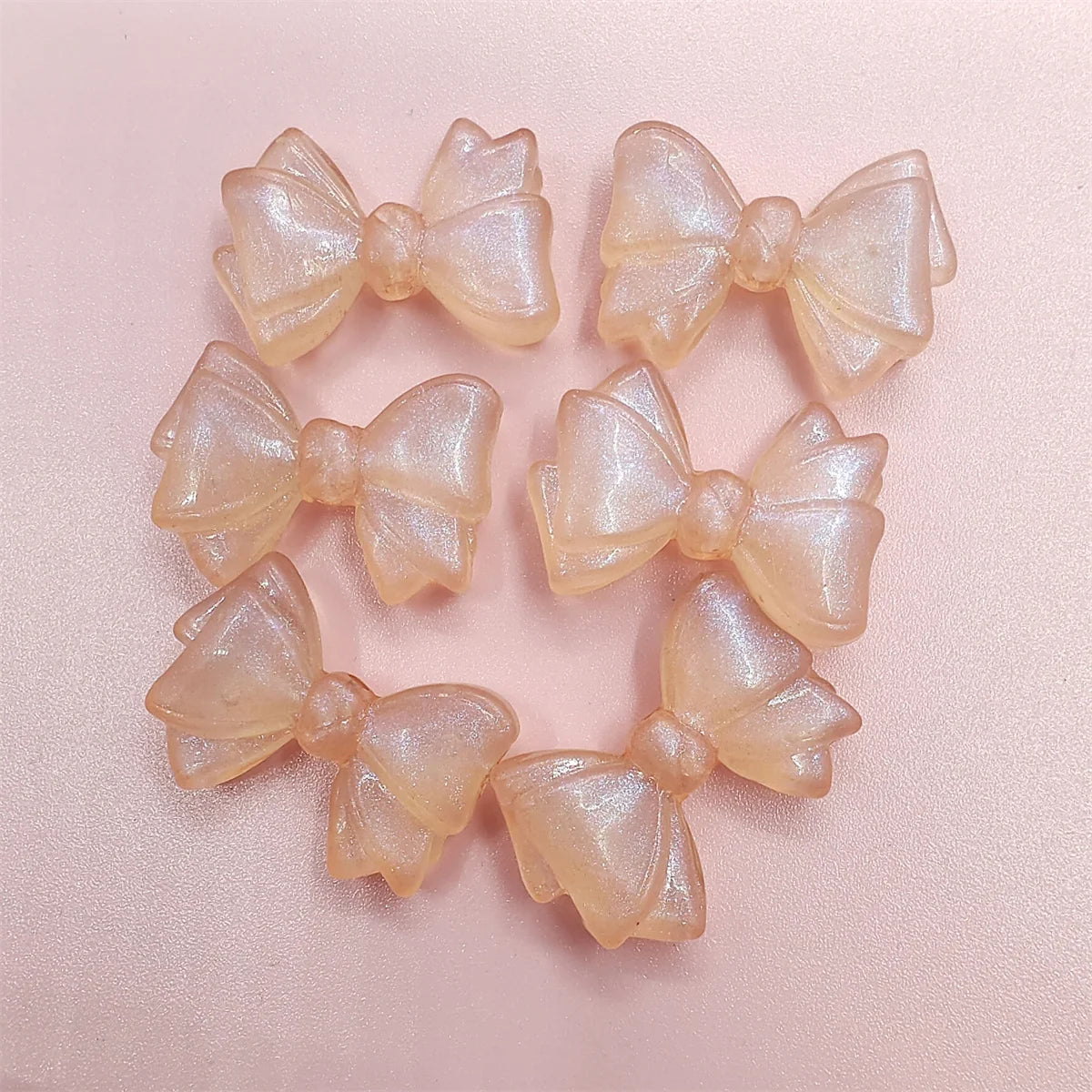A collection of translucent, pale pink shimmer mermaid bowknot beads for jewelry making.