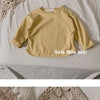 A yellow long sleeve cotton tee laid flat on a white surface next to a beige knitted item.