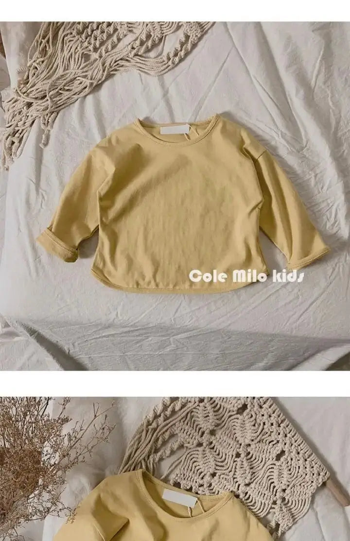 A yellow long sleeve cotton tee laid flat on a white surface next to a beige knitted item.