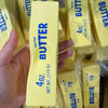A hand holds a yellow butter squishy stress relief toy packaged in clear plastic.