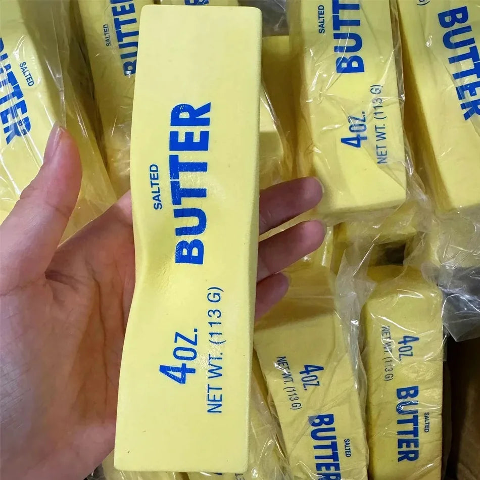 A hand holds a yellow butter squishy stress relief toy packaged in clear plastic.