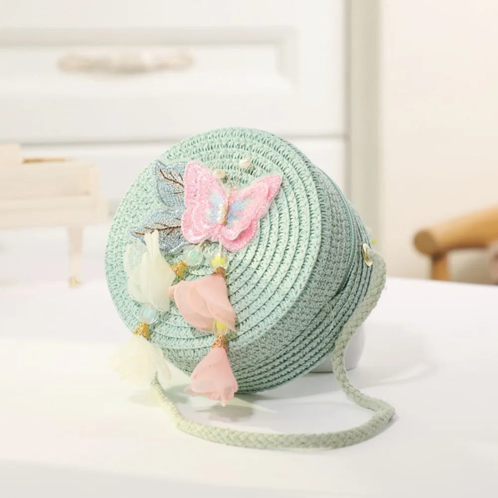A light mint green handwoven straw crossbody bag decorated with pink lace bows and floral accents.