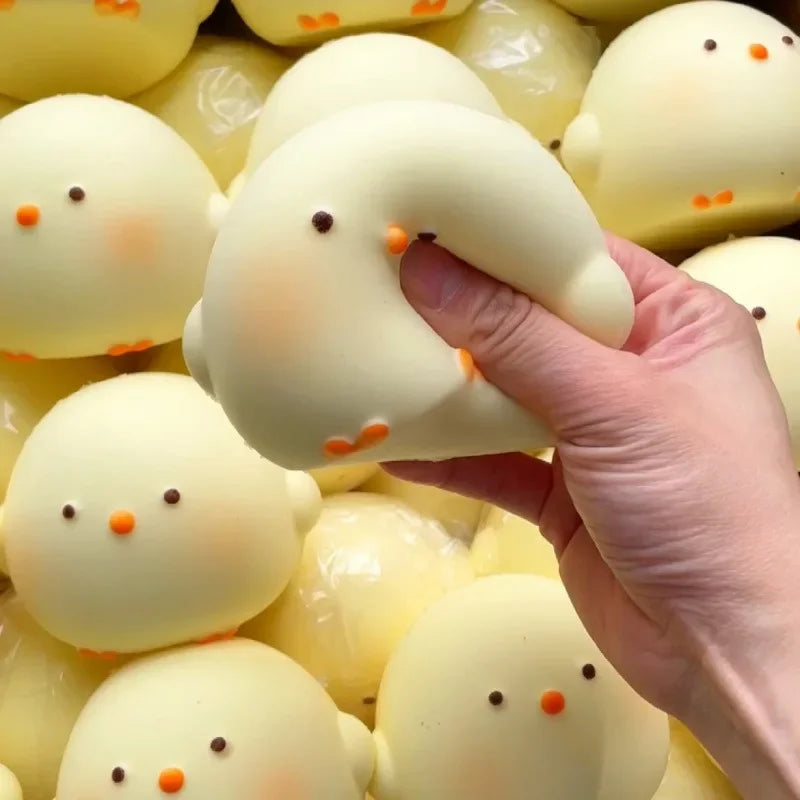 A hand is squeezing a yellow giant chick squishy toy, which is part of a collection.