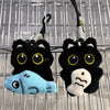 A black plush cat keychain charm with yellow eyes and a light blue accessory hanging from a metal wire grid.