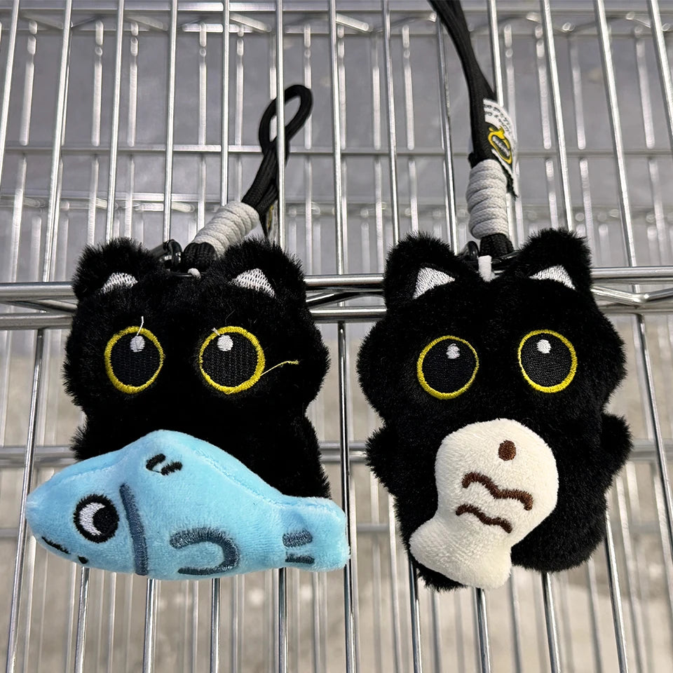 A black plush cat keychain charm with yellow eyes and a light blue accessory hanging from a metal wire grid.