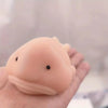 A hand holds a soft, pink squishy blobfish stress relief toy with a small black eye.
