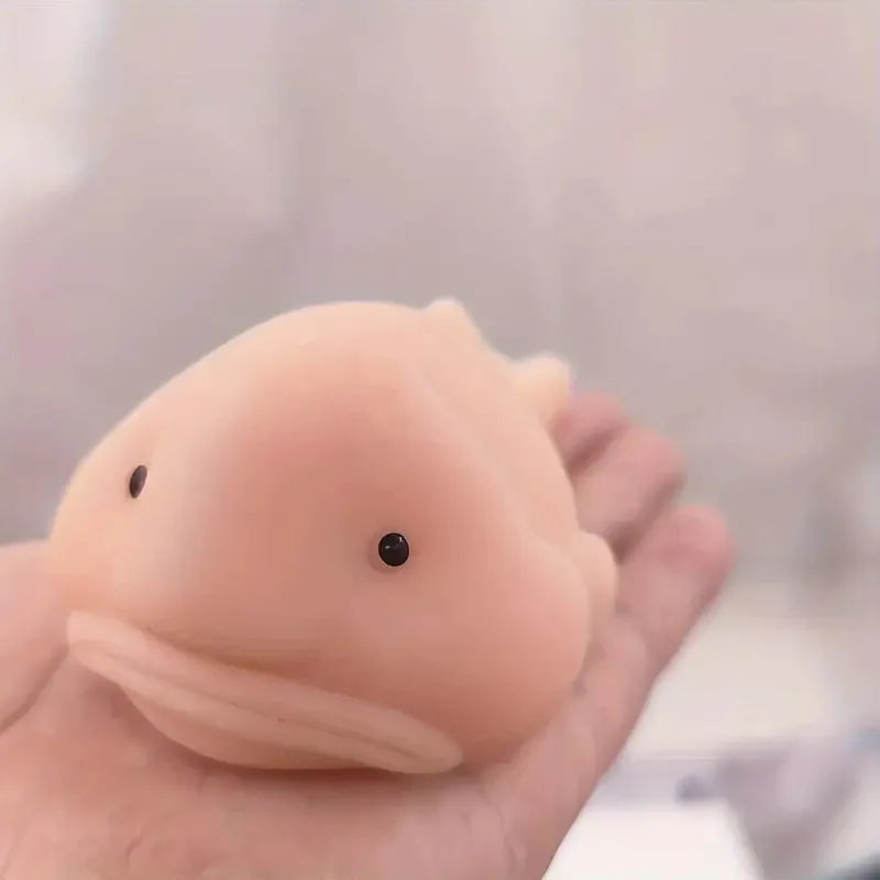 A hand holds a soft, pink squishy blobfish stress relief toy with a small black eye.