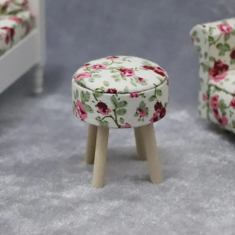 A small, round upholstered stool with wooden legs covered in a floral fabric for a dollhouse.