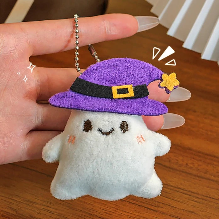 A white ghost plush toy wearing a purple witch hat with a black belt and gold accents, held by a hand.