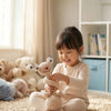 A young girl is sitting on a rug holding a handmade crochet sloth and squirrel plush toy.