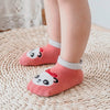 A pair of pink cotton cartoon panda socks with non-slip grips resting on a woven mat.