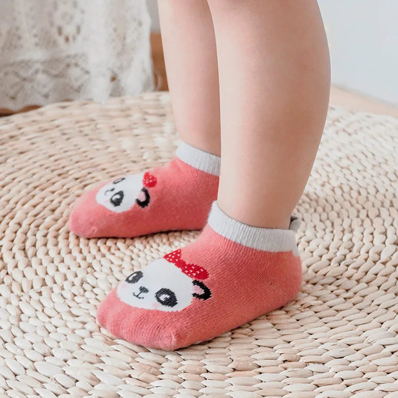 A pair of pink cotton cartoon panda socks with non-slip grips resting on a woven mat.