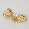 A gold-toned pacifier clip featuring a circular crystal design with the name Jose engraved on it.