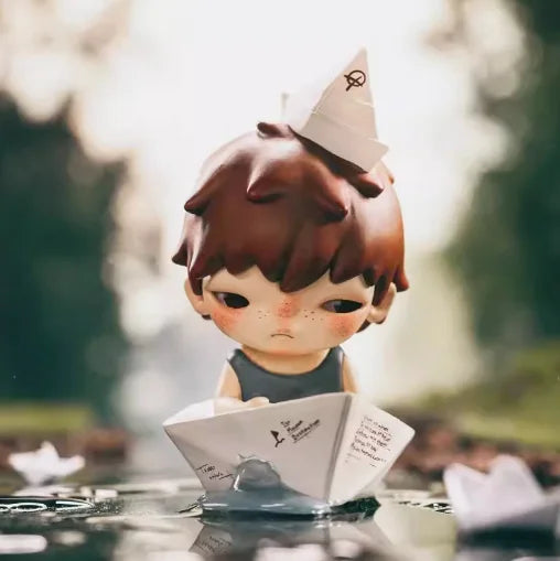 A small mischievous figure from the POP MART Hirono series is shown resting on a reflective surface.