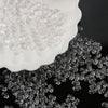 Clear oval glass rice grain beads scattered on a white plate and dark surface.