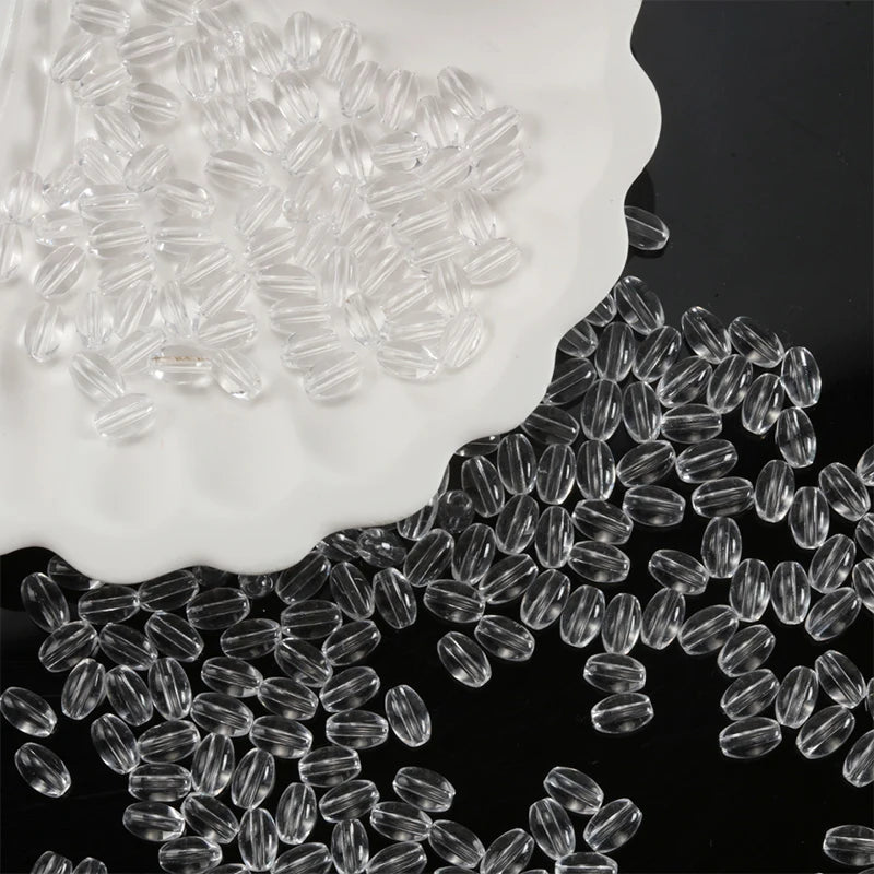Clear oval glass rice grain beads scattered on a white plate and dark surface.
