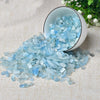 A small white bowl filled with light blue aquamarine chips scattered on a beige fabric.