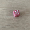 A single pink acrylic die with white dots is placed on a light wooden surface.