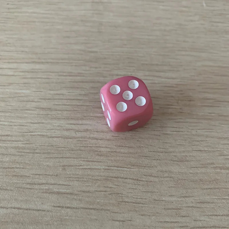 A single pink acrylic die with white dots is placed on a light wooden surface.