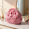A pink silicone mold shaped like a floral handbag rests on a marble surface next to a lit candle.