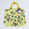 A yellow fabric tote bag featuring a green and yellow floral pattern with a gray hippo plush toy attached to the handle.
