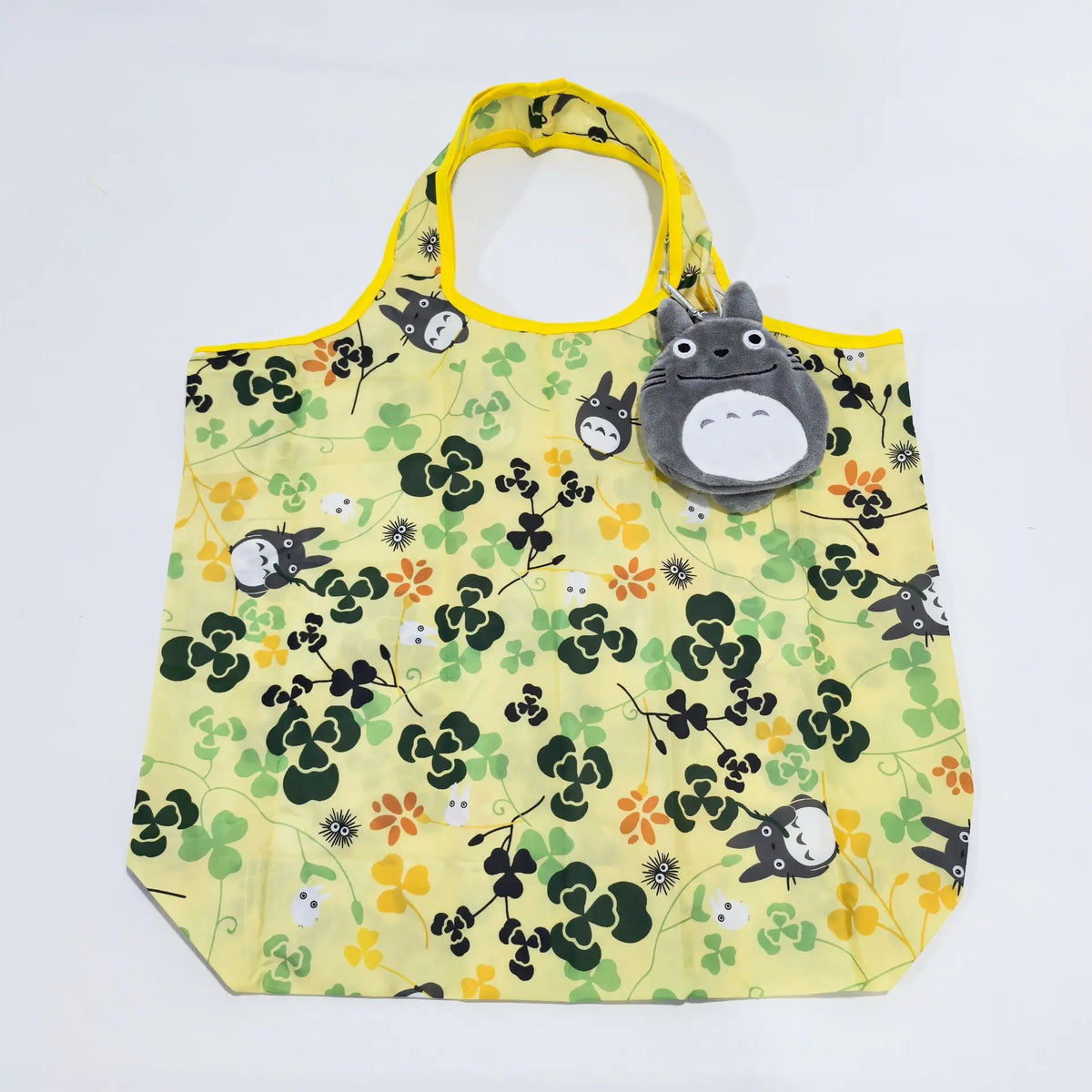 A yellow fabric tote bag featuring a green and yellow floral pattern with a gray hippo plush toy attached to the handle.