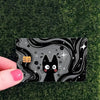A black cat face design with stars and swirls on a card skin sticker placed on green grass.