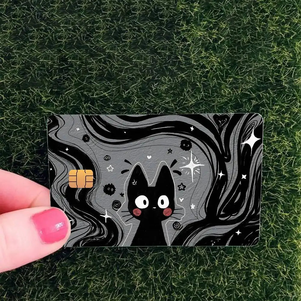 A black cat face design with stars and swirls on a card skin sticker placed on green grass.