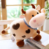 A soft, light brown cow plush toy with dark brown accents and pink nose, sitting on a white surface.