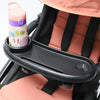 A pink and purple silicone bottle is placed in a black tray attached to a stroller seat.