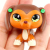 A small, brown miniature pet animal figure with orange fur and green eyes is held in a hand.