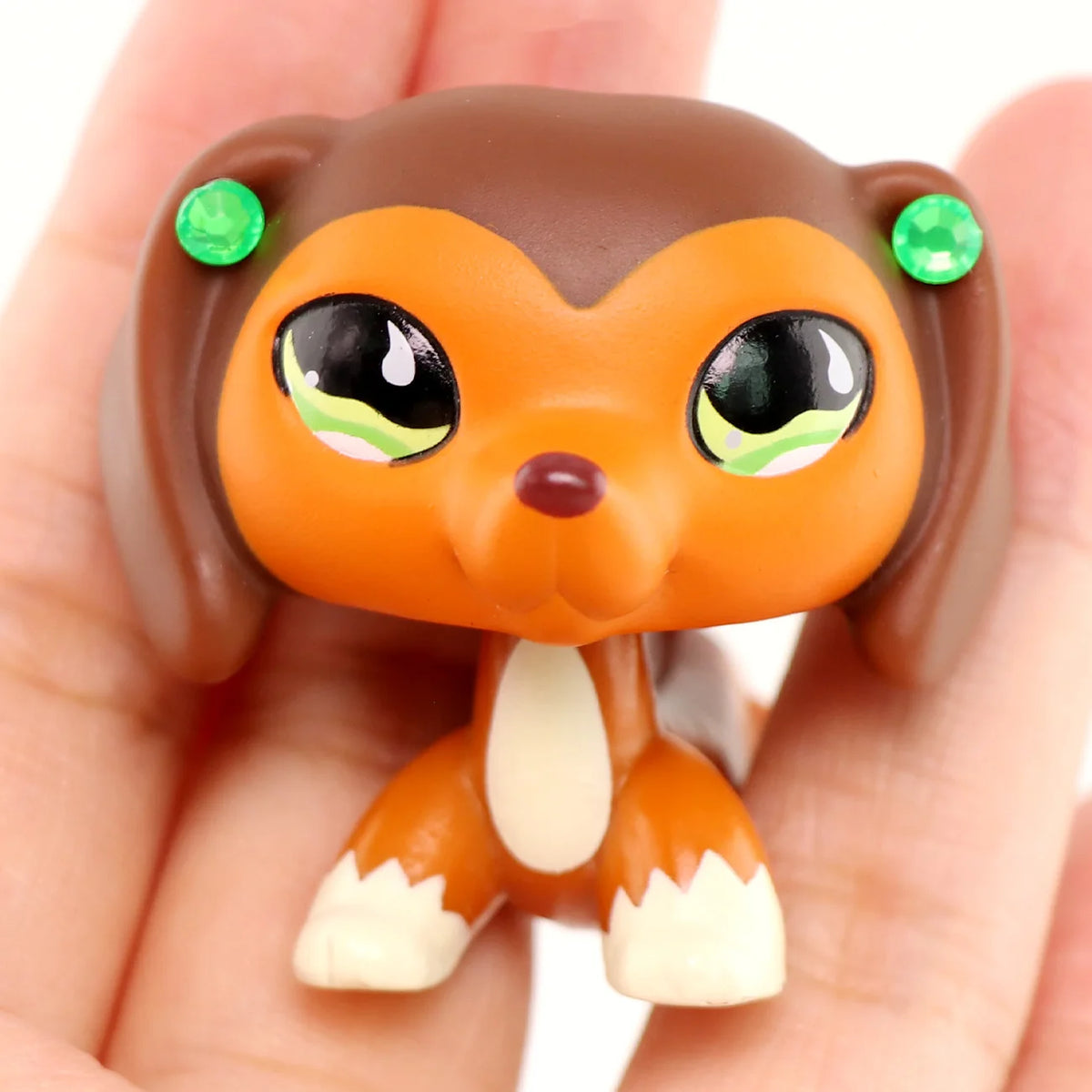 A small, brown miniature pet animal figure with orange fur and green eyes is held in a hand.