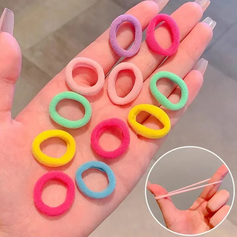 A hand displays a multi-pack of colorful nylon elastic hair ties in various shades of pink, purple, green, and yellow.