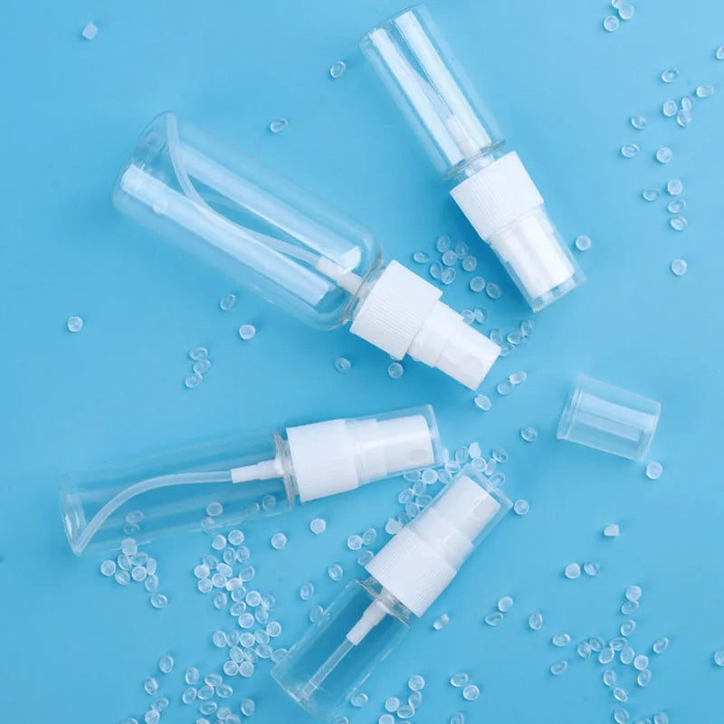 Three clear refillable travel spray bottles with white pumps scattered on a light blue background.