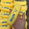 A hand holds a yellow butter stick squishy stress ball with the label 4oz butter salted.