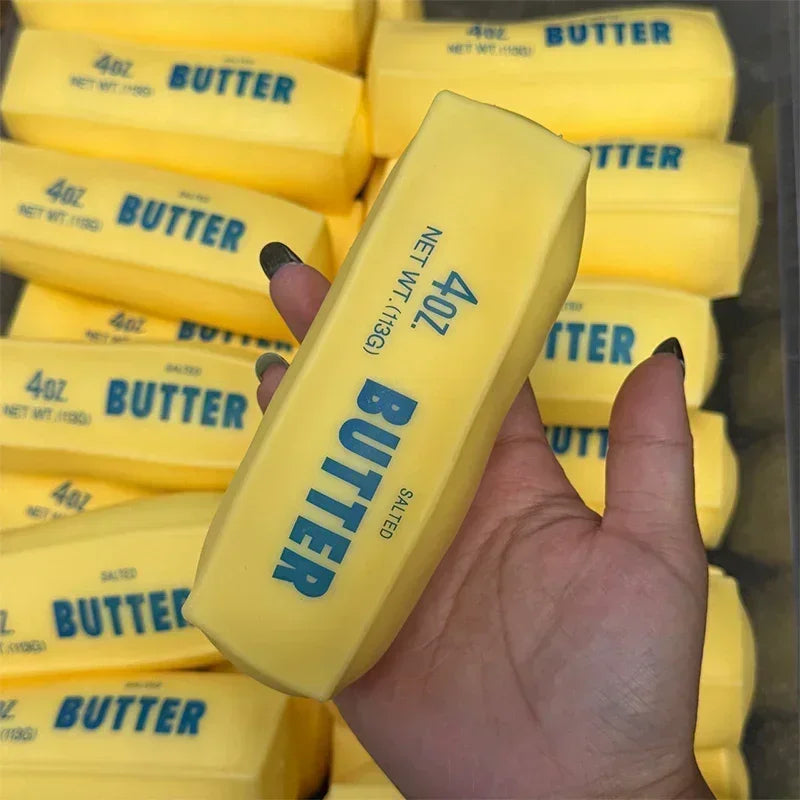 A hand holds a yellow butter stick squishy stress ball with the label 4oz butter salted.