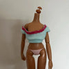 A brown doll with a light blue top and pink trim, wearing pink panties.