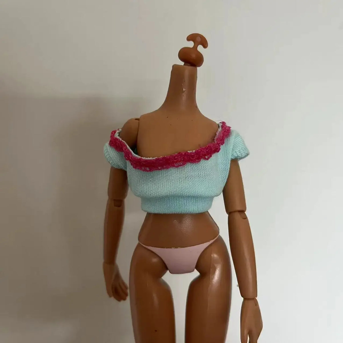 A brown doll with a light blue top and pink trim, wearing pink panties.