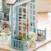 A miniature wooden dollhouse kit featuring a blue and white structure with furniture and a yellow animal figure.
