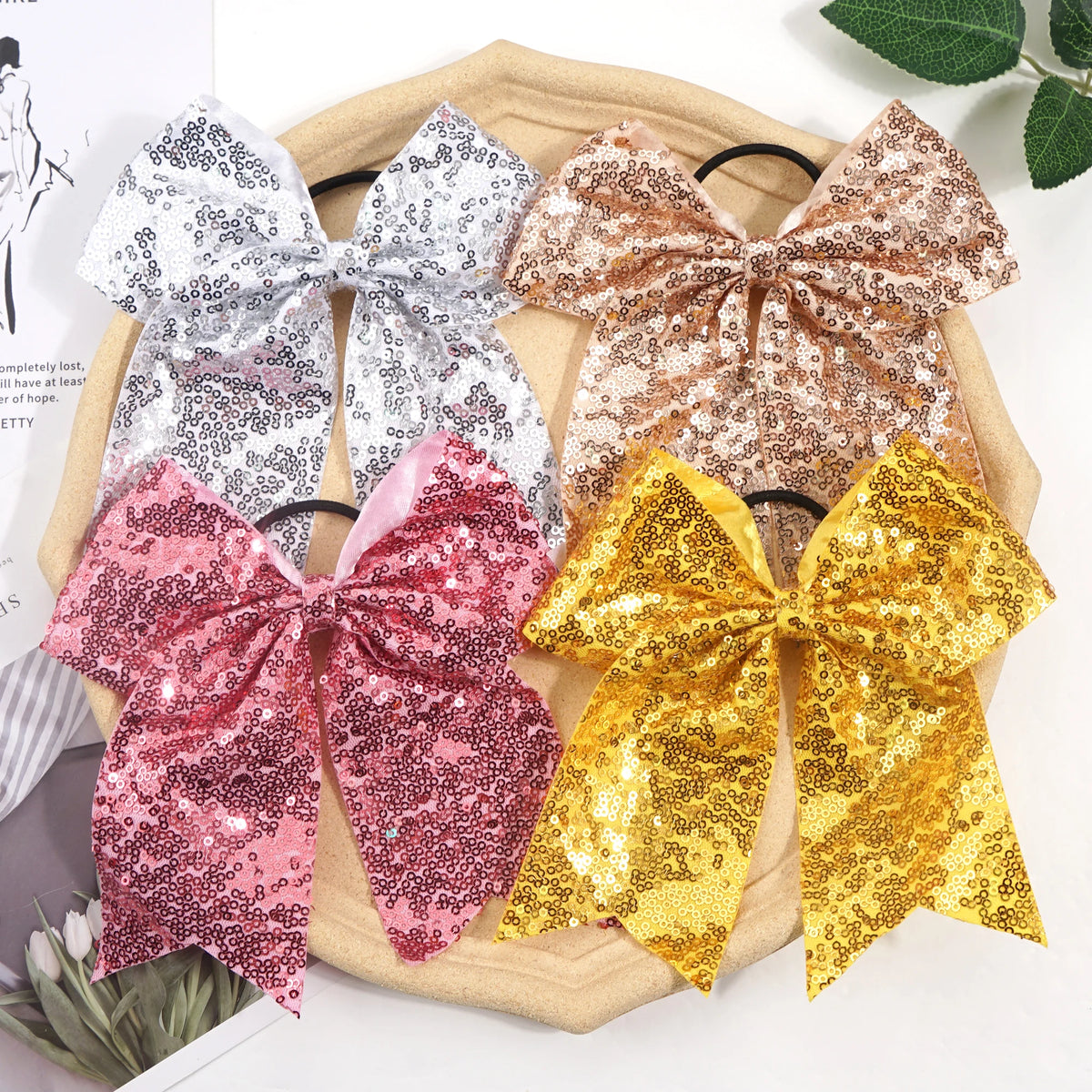 A collection of five glitter sequin pigtail bows in pink, silver, bronze, and gold are displayed on a wooden tray.