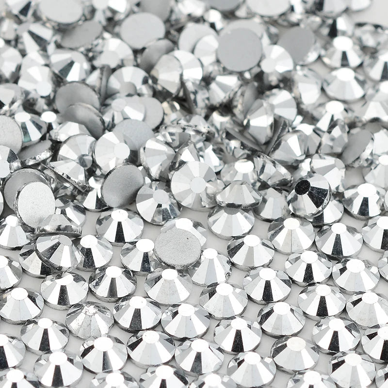A close-up view of small, silver glass crystal flatback rhinestones scattered on a white background.