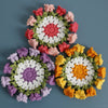 Hand-crocheted lily of the valley coasters featuring colorful floral patterns in pink, white, purple, and orange.