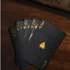A stack of dark gray frosted poker playing cards showing the Ace through Jack, resting on a wooden surface.